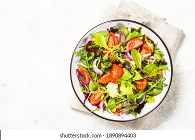 Green salad from fresh salad leaves and vegetables in white plate. Healthy vegan food. Top view image.