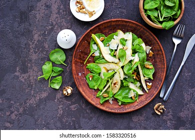 Green salad of fresh spinach, juicy pear, walnuts and parmesan on a brown clay plate on a dark concrete background. Vegan recipes. Healthly food. Copyspace. - Shutterstock ID 1583320516