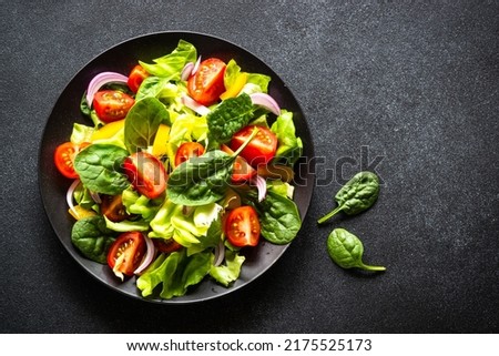 Green salad with fresh vegetables and green leaves at black background.