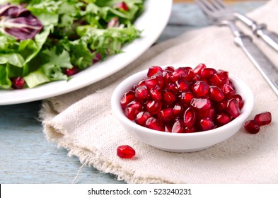 Green salad with spinach, frisee, arugula, radicchio and pomegranate seeds on blue wooden background.
