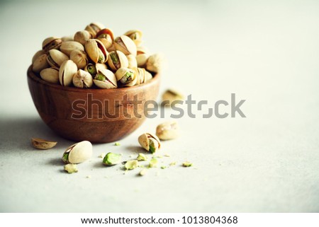 Green salted pistachios in wooden bowls on light concrete background. Copy space for your text. Healthy nuts snack. Banner.