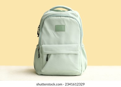 Green school backpack on white grunge table near yellow wall