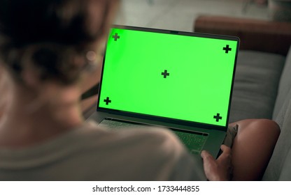 Green Screen Mock Up Girl Sitting On Sofa And Continuously Watching On Laptop Screen In Cozy Evening Room