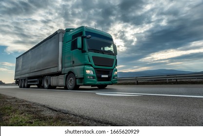 Green Semi Trailer Truck Driving On A Highway With Dramatic Sunset Sky In The Background. Transportation Vehicle