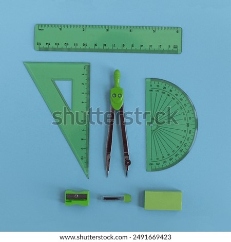 green set of geometry tools with compass, rulers, eraser and sharpener lie on a blue background, top view. Mathematics and study