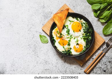 green shakshuka in a cast iron skillet. fried eggs with spinach and fried toast. healthy nutritious breakfast,