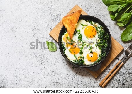 green shakshuka in a cast iron skillet. fried eggs with spinach and fried toast. healthy nutritious breakfast,