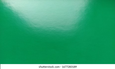 Green Sheet Of Shiny Colored Paper. The Reflective Surface Glares In The Light. Bright Intense Color. Beautiful Background. Highlight On Top. Green Turning Into Blue. Gradient.