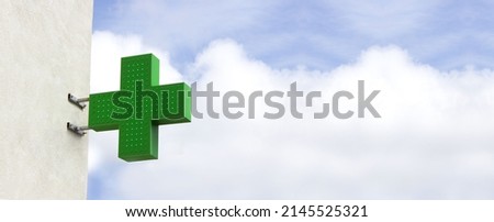 Green shining medical cross indicating the location of a pharmacy on street. Banner medical cross on sky background
