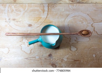 Green side handle bowl pitcher of almond milk, centered, very long wooden spoon with single almond balanced on top, horizontal aspect