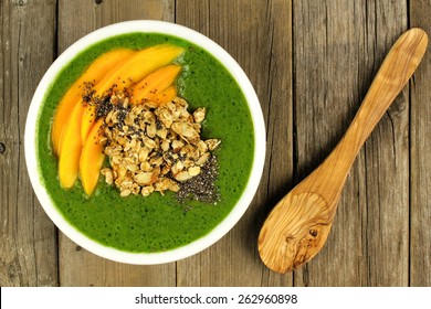 Green Smoothie Bowl With Mangoes, Granola, Almonds And Chia Seeds, Overhead View On Wood With Spoon