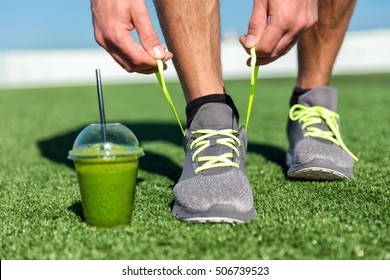 Green smoothie fitness man lacing running shoes, Athlete runner with green vegetable detox juice getting ready for morning run tying running shoe laces on grass. Fitness and healthy lifestyle concept. - Powered by Shutterstock