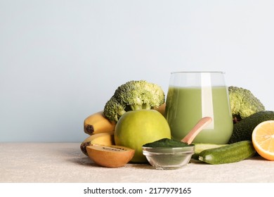 Green Smoothie In Glass, Spirulina Powder, Vegetables And Fruits On Blue Background. Healthy, Raw, Vegan Diet Concept. Copy Space