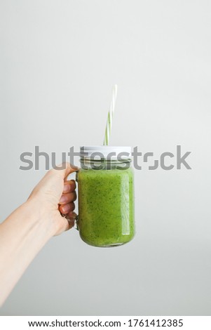Green smoothie in a mason jar with white lead and recycled paper straw. Summer refreshments. Spinach and cucumber smoothie.