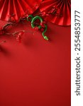 Green snake winding around branches with red flowers on a red background with decorative paper fans. Chinese New Year 2025 concept