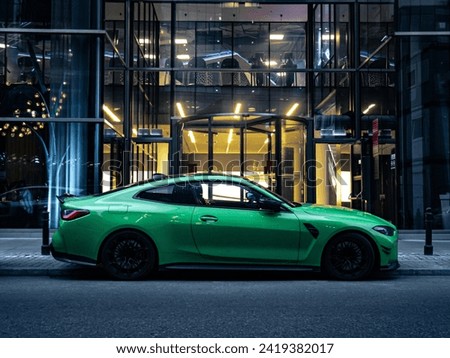 Green sports car parked in front of a modern building, evening side shot of car