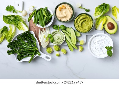 Green spring vegetable appetizer platter with dips. Healthy crudites snack board on white marble background. 