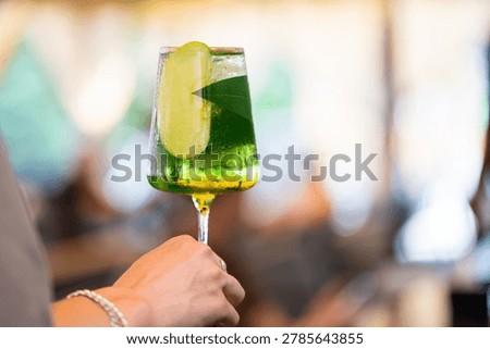 Green spritz cocktail with a slice of green apple and leaf in a wine glass held by a hand.