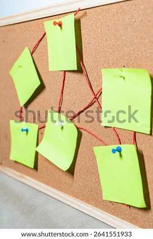 Green sticky notes connected with red thread on pink cork board for brainstorming and planning