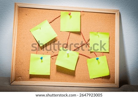 Green sticky notes connected with red thread on pink cork board for brainstorming and planning