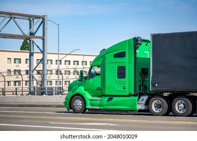 Green Stylish Bonnet Big Rig Semi Truck Tractor With Sleeping Cab Compartment For Truck Driver Rest Transporting Cargo In Black Covered Semi Trailer Running On The City Street Bridge