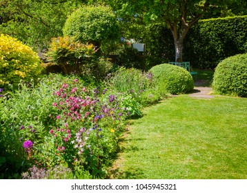 Green Summer Walled English Formal Garden With Lawn Blooming Flowers And Hedgerow In Background, Southern England, UK