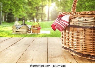 Green Sunny Day In Park And Red Napkin Wooden Table And Picnic Basket 