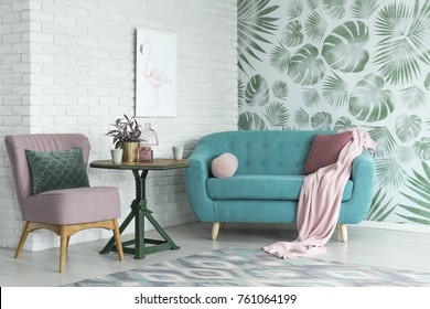 Green table with a plant between pink chair and blue sofa in floral living room with wallpaper and poster - Shutterstock ID 761064199