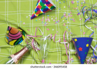 Green Tablecloth After A Party Celebration With Confetti, Empty Bottle And Glass Of Champagne And Party Popper.