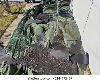 A Green Tarp Covering A Garden Area With A Bunch Of Old Shingles Lying On It.