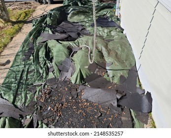 A Green Tarp Covering A Garden Area With A Bunch Of Old Shingles Lying On It.