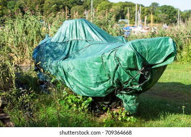 Green Tarp Covering A Small Boat On Land.