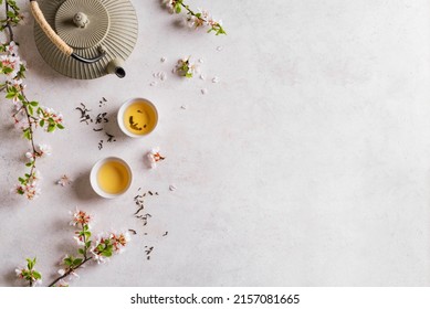Green Tea and Cherry Blossom on white table, top view, copy space. Japanese cast iron teapot and cups, asian green tea composition with sakura bloom and petals. - Shutterstock ID 2157081665