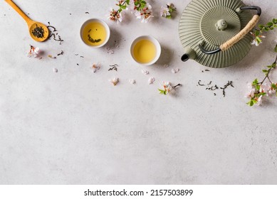 Green Tea And Cherry Blossom On White Table, Top View, Copy Space. Japanese Cast Iron Teapot And Cups, Asian Green Tea Composition With Sakura Bloom And Petals.