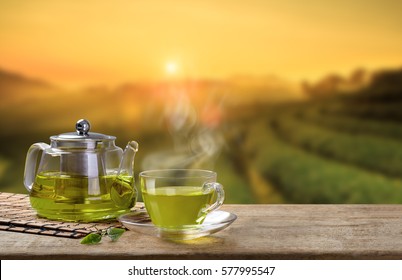 Green Tea Cup And Glass Jars With Fresh Green Tea Leaves On The Wooden Table And The Tea Plantations Background With Copy Space