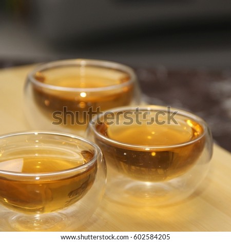 Green tea in a glass transparent bowl. Few small cups of tea on wood. Glass piala with double walls, double-bottomed bowl. Meal, aperitif, repast. Square