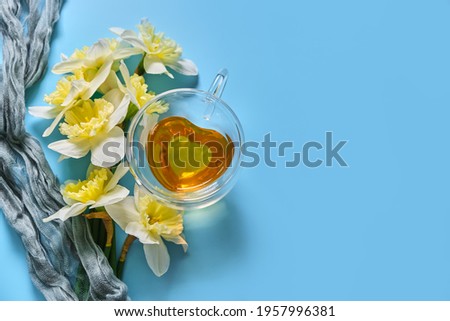 Green tea in a in a heart-shaped glass cup with a double bottom on the napkin with daffodil flowers on blue backgound. Spring still life.