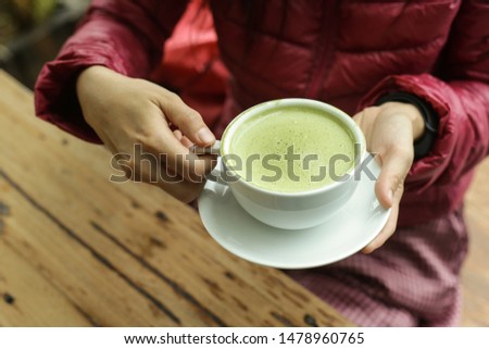 Green tea,  hot matcha latte in white ceramic cup with saucer on young woman hand with cinnamon