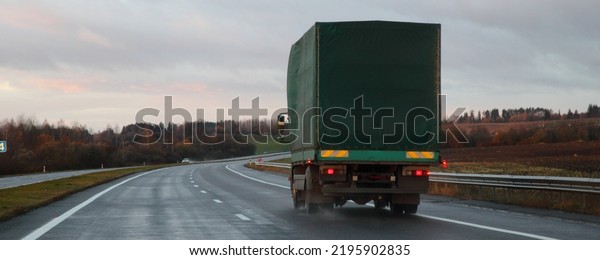Green tented truck drive on suburban wet asphalted\
highwayroad back view at autumn day, safety driving on rainy\
slippery road