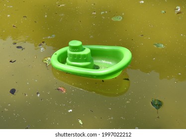 Green Toy Plastic Boat In Small Pond With Green Water And Plant Debris. Pond Of The Laundry Of The Village Of Armejún, Province Of Soria, Spain.