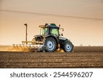 Green tractor seeding soil with planter in agricultural field during golden hour