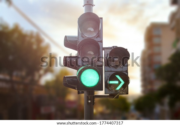 Green traffic light with green arrow\
light up in city while sunset allows car to turn\
right
