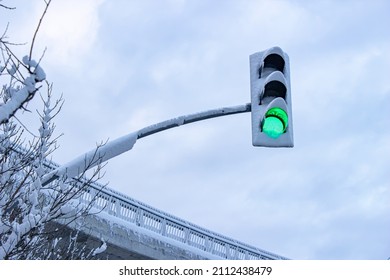 Green traffic light, bridge and tree covered with snow and cloudy sky in the background. - Shutterstock ID 2112438479