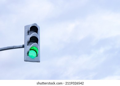 Green traffic light covered with snow and cloudy sky in the background. - Shutterstock ID 2119326542