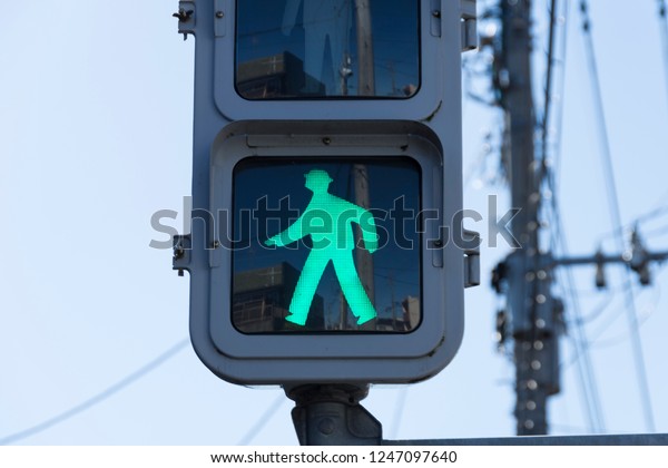 A green\
traffic light sign that says people can walk or pedestrian walking.\
This traffic sign was taken in Japan. \
