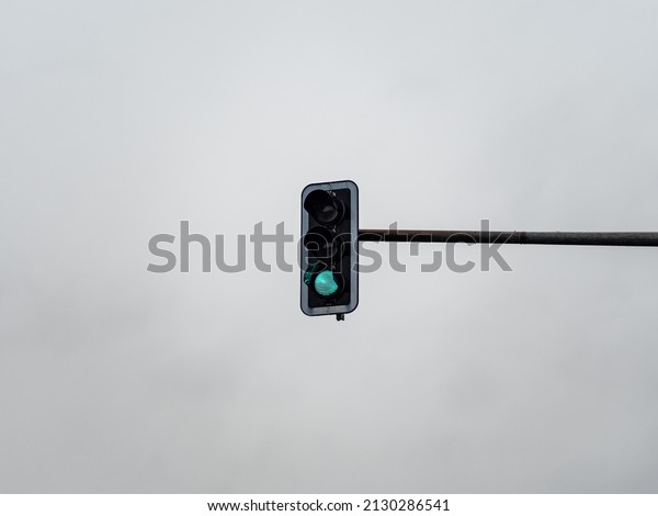 Green traffic light signal in\
front of an overcast sky. Light symbol to control the cars on the\
street and to guide the road user. Go sign to regulate the\
traffic.