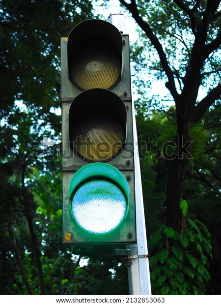 A green traffic light that lights
up, it means that all vehicles all vehicles can pass on the road.
Photographed during the day with trees in the
background