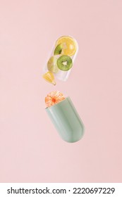 Green Transparent Pill With Lemon, Tangerine, Kiwi And Lime On Isolated Pastel Coral Pink Background. Minimal Pharmaceutical Abstract Concept Of Supplements. Natural Fruit Sources Of Vitamin C.