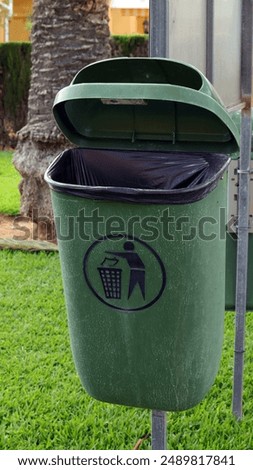 Green trash can with open lid on metal rail isolated on green landscape background close-up