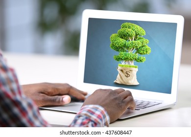 Green tree in bag with a dollar sign in screen of laptop and businessman - Powered by Shutterstock